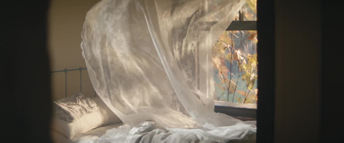A sheer curtain billows out over the bed as the wind blows through the window