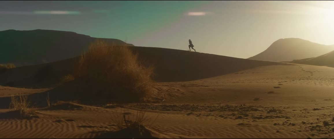 A woman is running on a hill in the desert as the sun shines brightly in the sky