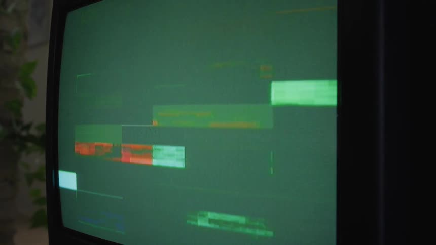 Rectangular shapes flicker on and off television screen as houseplant vines hang down in background