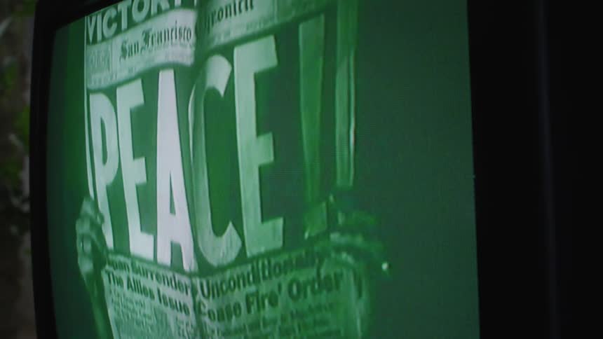 Man holding up newspaper saying peace in the headline on old television