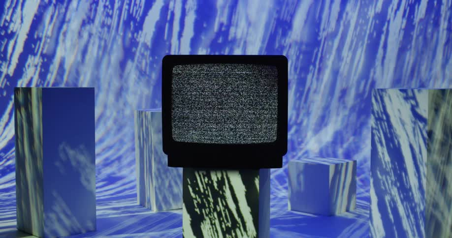 A television set with a fuzzy screen sits on a block in a room with lights moving on all the walls