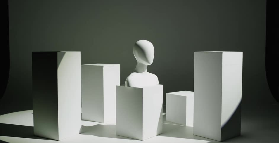 Spotlight flows across mannequin bust and several various sized blocks brightening the area before leaving it in darkness