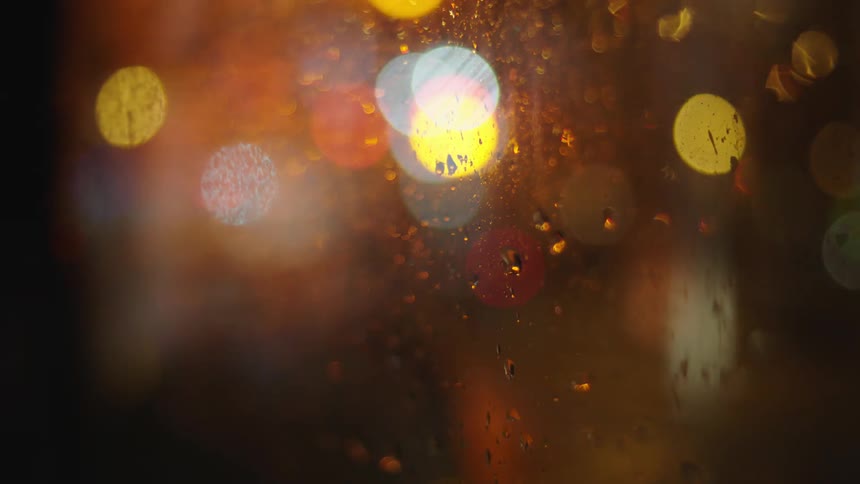 Raindrops on glass distort the image of traffic and lights outside