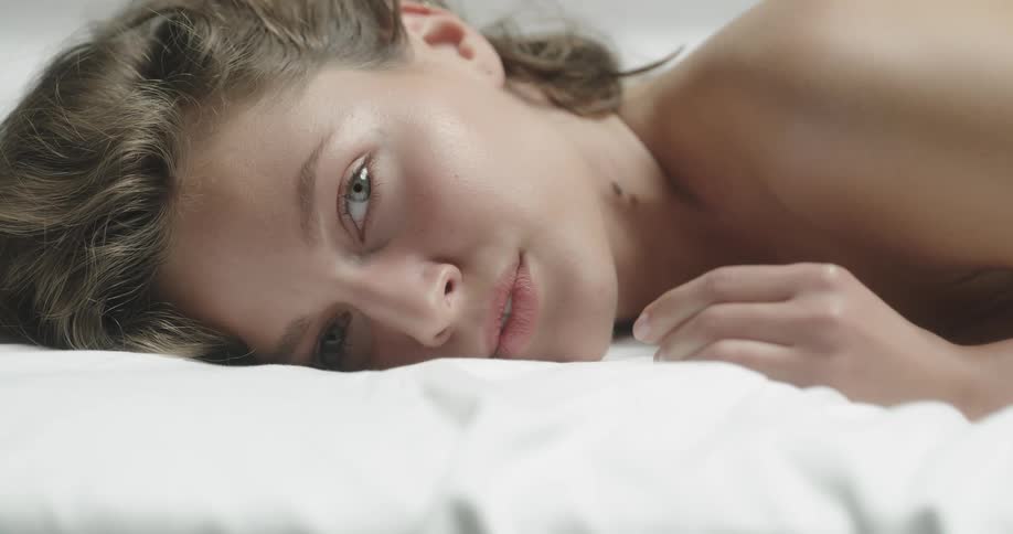 Topless female model with brown wavy hair lies in prone position smiling