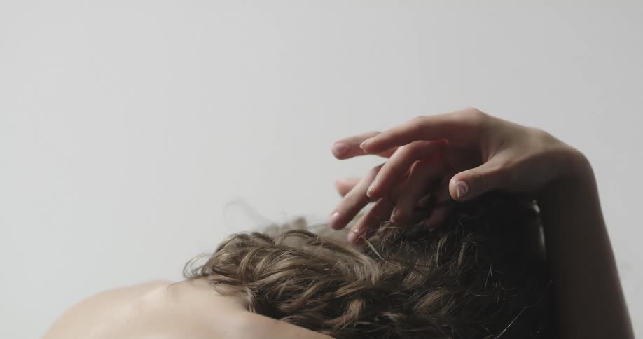 A woman sitting with her head completely bowed forward running her fingers through her hair