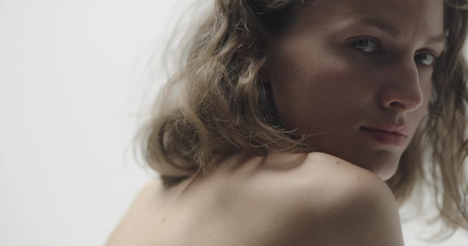 Topless female model with brown wavy hair looks over her shoulder
