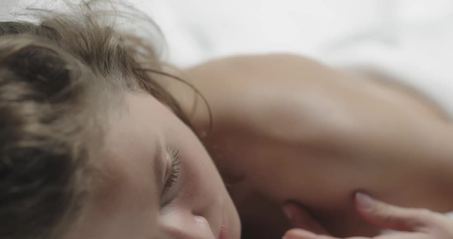 A woman rubs her shoulder while lying facedown in bed