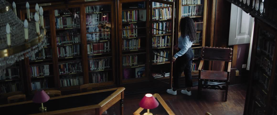 A woman gets up from a desk in a library and walks over to a cabinet to select a book