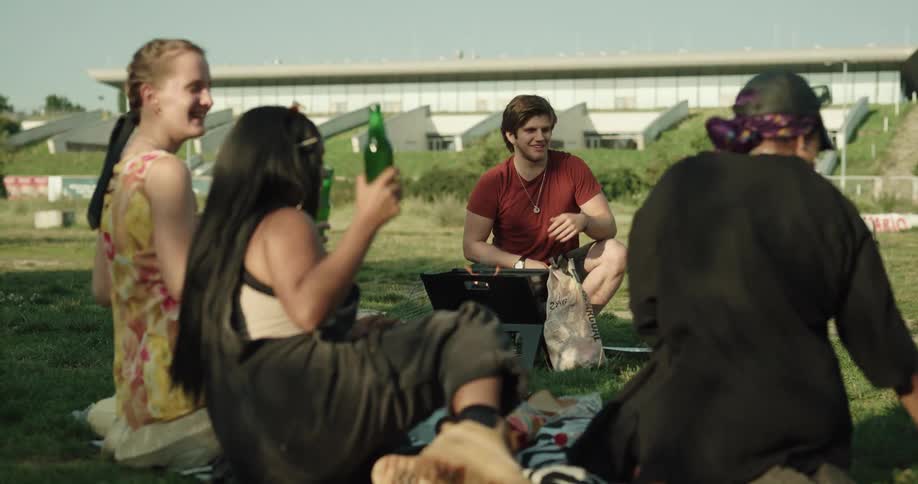 A man unpacking beer bottles at a picnic tosses a bottle to a friend