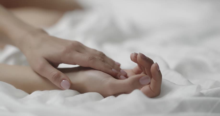 A woman runs her fingers down her wrist while lying in bed