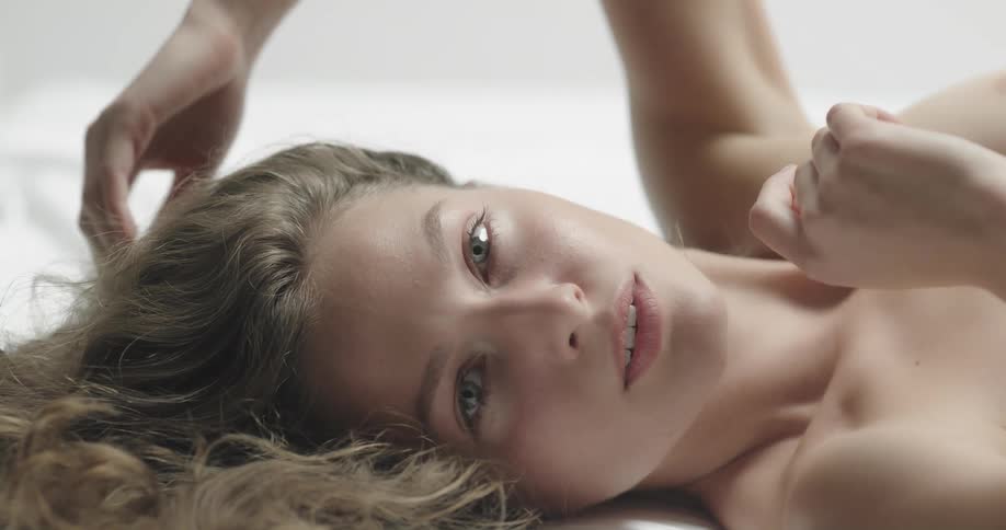 Shirtless female model lies down on ground touching her brown wavy hair
