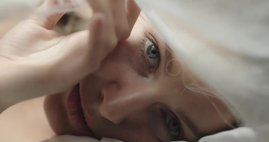 Woman lying on bed lifts fabric from over her face and smiles
