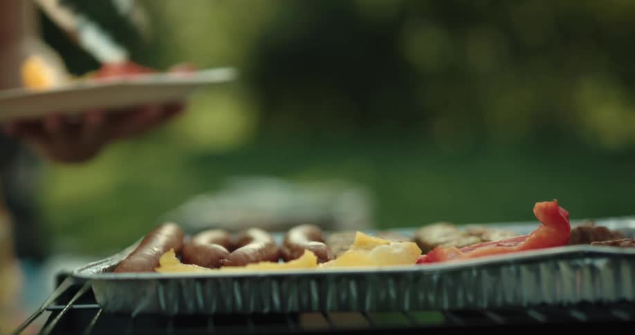 A person puts food on a grill outside to cook