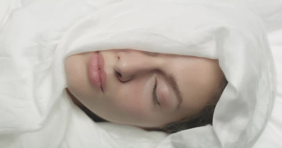 A woman lies in bed with a sheet covering half of her face