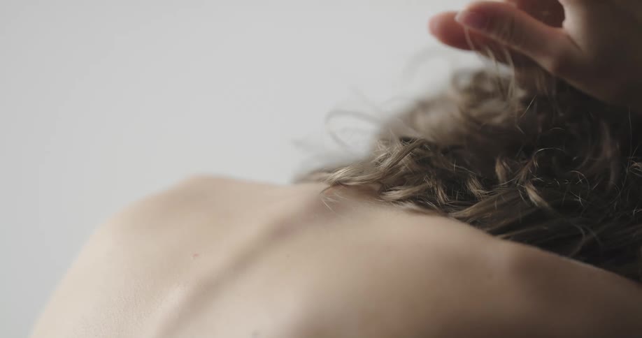Topless female model with brown wavy hair crouching and touching wavy hair