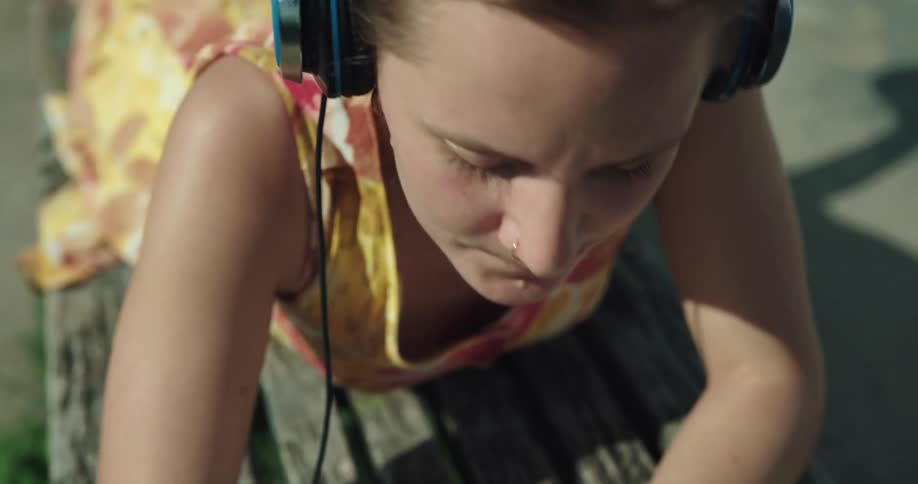 Woman with yellow dress headphones lies in prone position on bech writing down in notebook