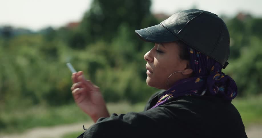 Woman wearing leather cap relaxing smoking cigarette outdoors in nature