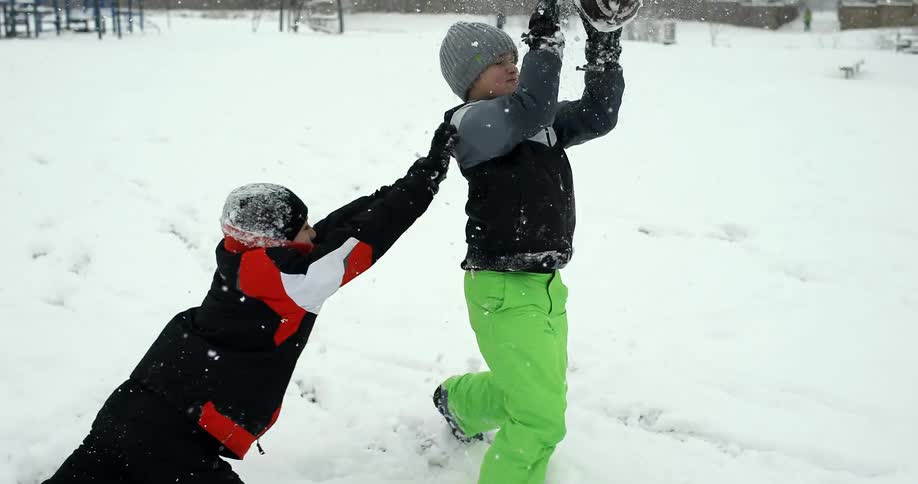 A boy running in the snow catches a football and is tackled