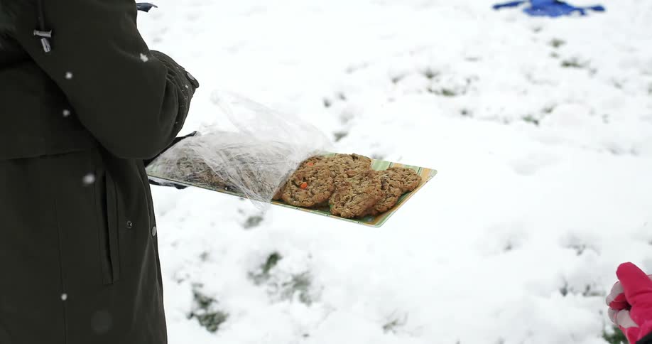A gloved hand pulls plastic wrap back from a plate of cookies while it snows