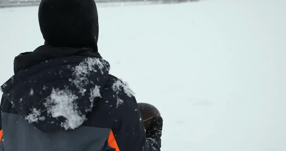 A boy is tossing a football as he walks in the snow