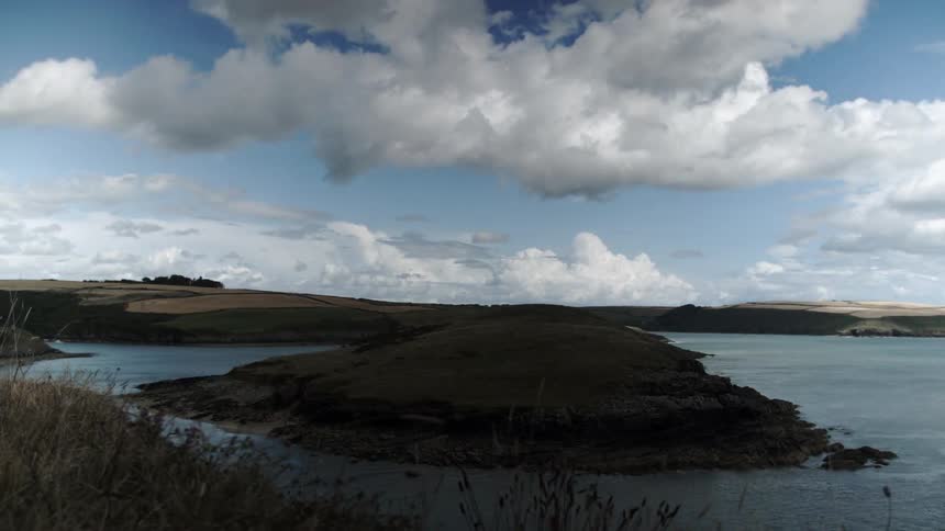 Clouds flow in the sky over a hilly landscape and a body of water