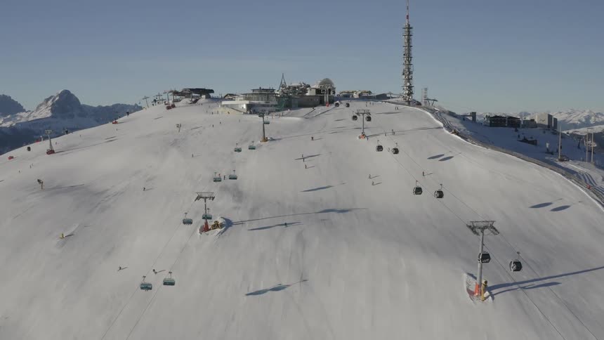 Skiiers descend a ski slope beneath a ski resort on a mountain during the day
