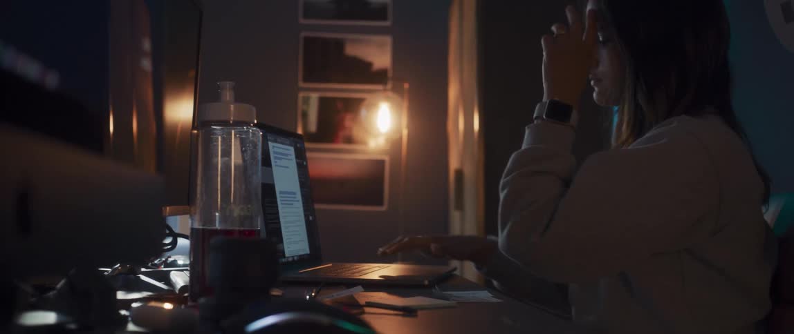Woman sits in dark office at night working on laptop