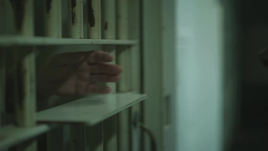 An inmates hand is sticking out of prison bars as a guard removes their handcuffs