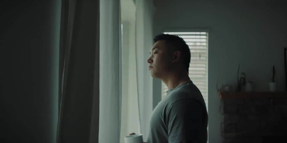 A man holding a mug standing at his window looking out taking deep breaths