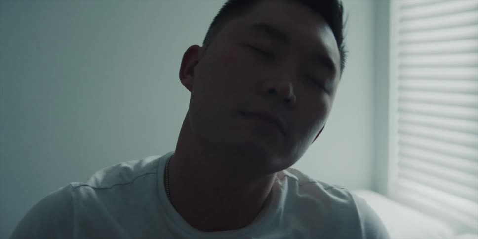 A man sitting on his bed rolling his head stretching his neck