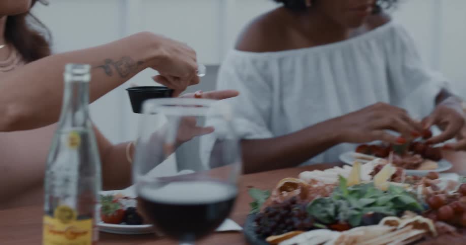 Friends eat from platter at wooden table while they laugh and talk