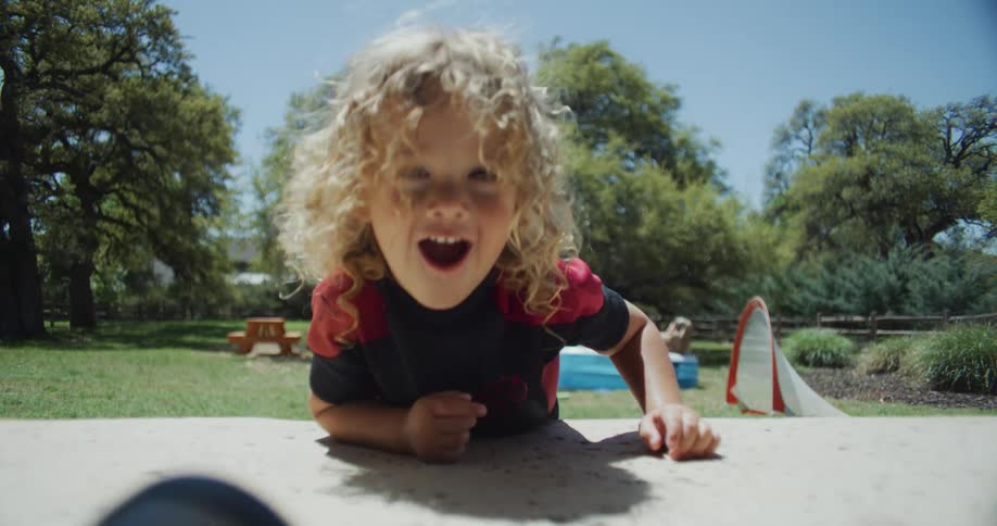 A child laughs and giggles as he tosses a plastic cup across the table in the backyard