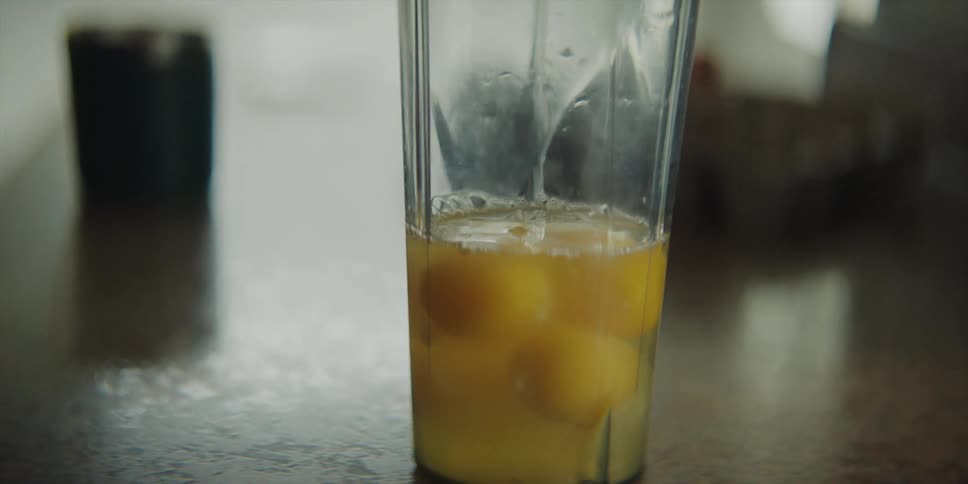 A man cracks an egg on the counter and adds it to a plastic tumbler