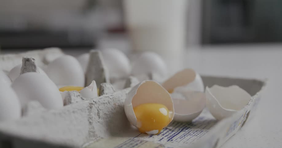 A egg yolk sits in a broken shell in an egg carton