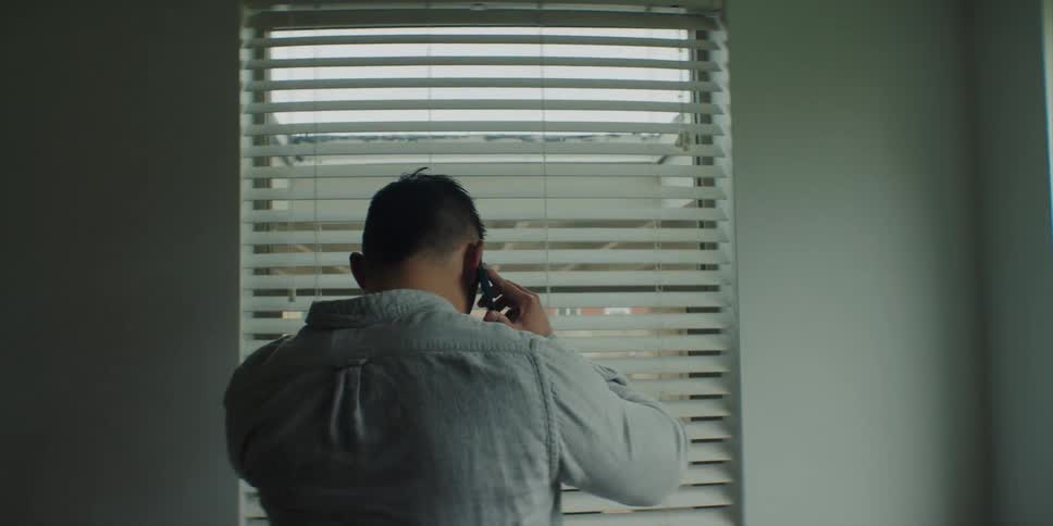 A man is talking on the phone and standing near a window