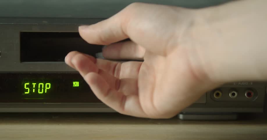 A persons hand is seen putting a tape in a vhs player