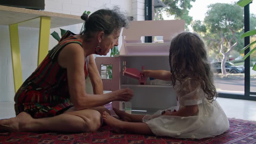 A grandmother and granddaughter play with the doll house
