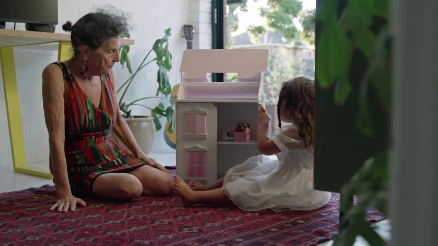 Grandmother and granddaughter play with dollhouse while sitting on floor
