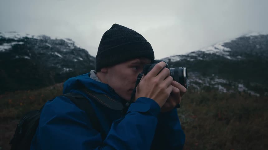 A photographer raises a camera to his face to take photographs in the mountains on a cloudy day