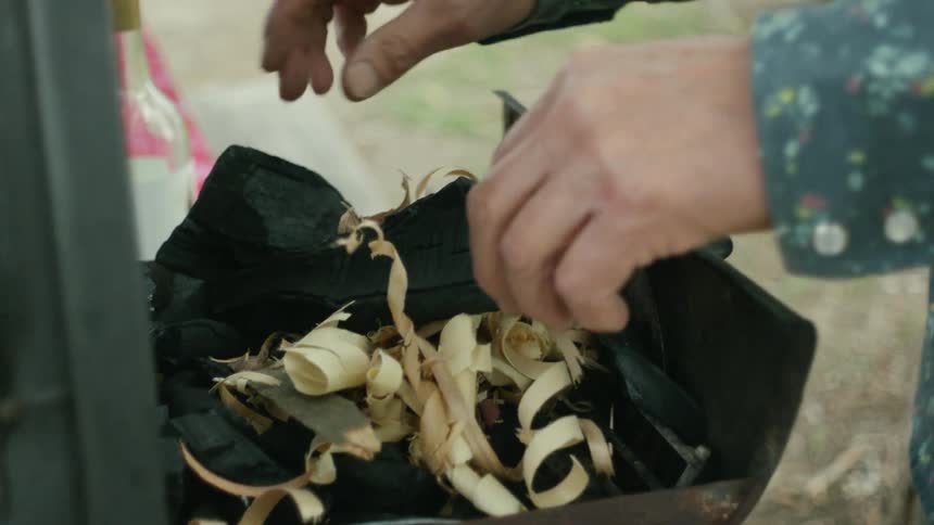 A man adds wood shavings to a smoker