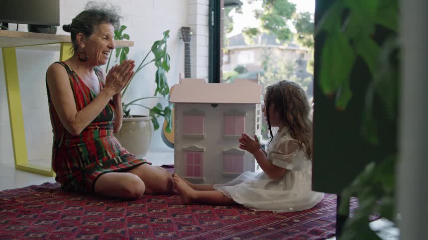 A woman is sitting on the floor playing with her granddaughter