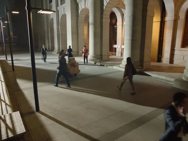 A woman delivering packages checks her watch then begins to run past business people pushing her cart