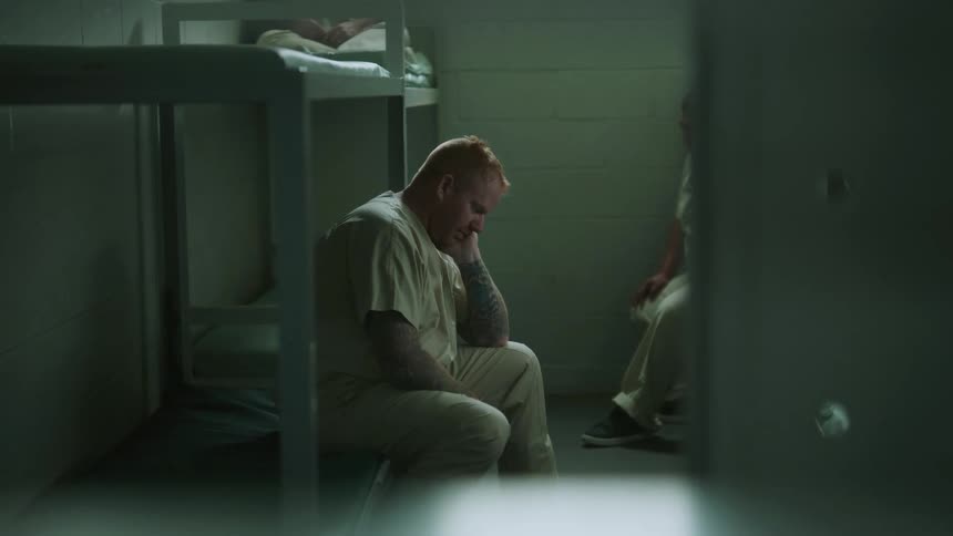 A man sits with his head bowed in the bottom bunk of a jail cell