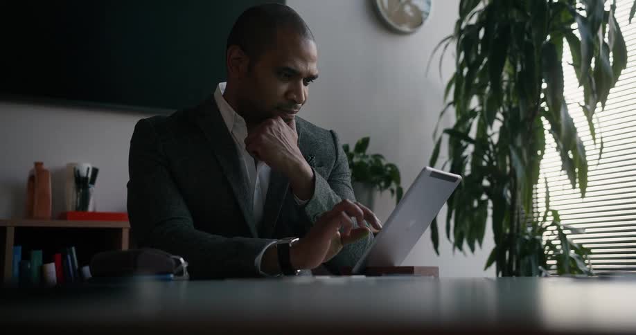 Businessman with blazer jacket and wristwatch sits at table using tablet