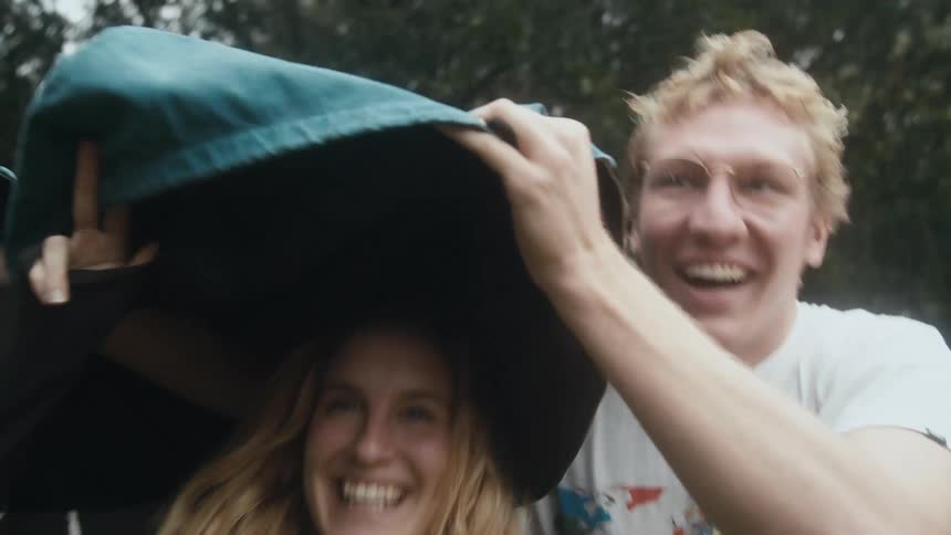 A man covers a womans head as they run through the rain