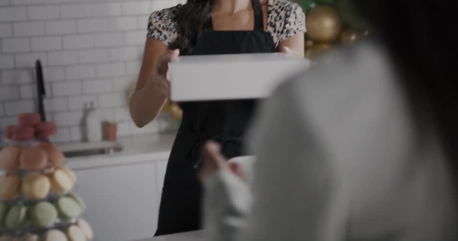 A bakery employee hands a customer a box of desserts