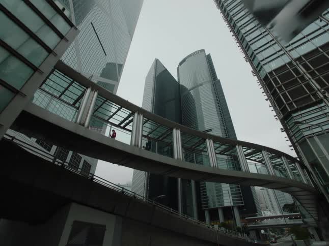 People walk and run across the skywalk between skyscrapers in hong kong on a gray foggy day