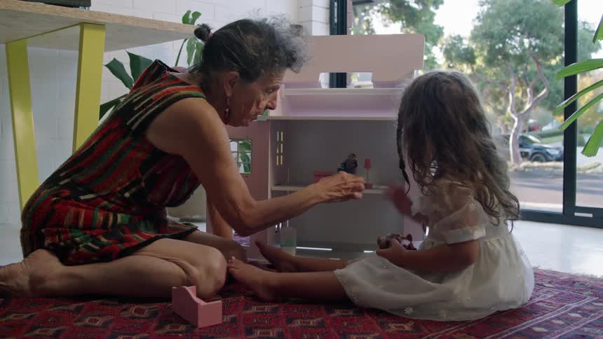 A girl and her grandmother play with dolls on the floor