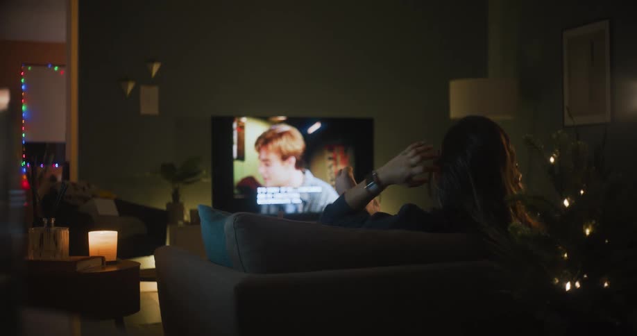 A woman sitting in a comfy chair playing with her hair and flexing her toes while watching tv