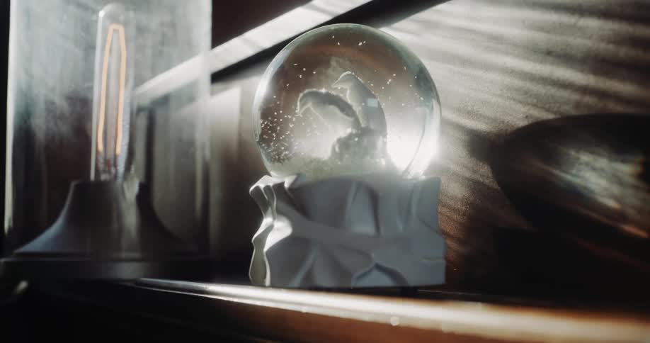 A snow globe featuring a family of penguins sits on a fireplace mantel